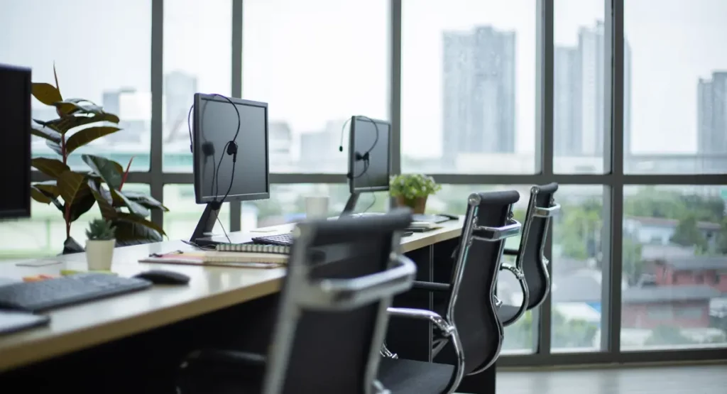 Unbesetzte Arbeitsplätze in einem modernen Büro, in dem Desk Sharing betrieben wird. Hinter der Fensterfront sind weit entfernt Hochhäuser zu sehen.