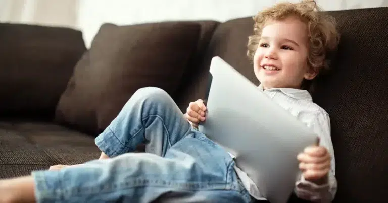 Ein Junge der Generation Alpha liegt mit einem Tabelt auf einem Sofa